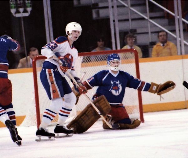 Edmonton Oilers center Steve Carlson, who appeared in the movie Slap Shot as one of the three Hanson Brothers, camps out in front of Birmingham Bulls goalie Pat Riggin in WHA action.